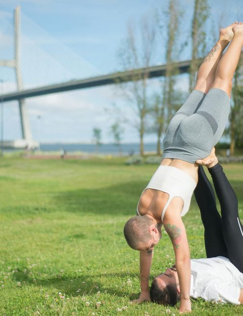 Couple in a partner yoga pose, demonstrating balance and mutual support in a green-tinted atmosphere.